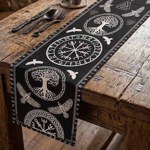 May include: A black table runner featuring white printed designs of the Vegvisir compass, the Yggdrasil tree of life, flying ravens, and triangular knotwork symbols. The edges are bordered by a continuous pattern of runic characters.