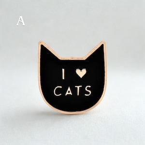Könnte beinhalten: Eine schwarze, katzenförmige Anstecknadel mit goldenem Rand. Auf der Anstecknadel stehen die Worte "I ❤️ CATS" in goldener Schrift. Das Herzsymbol ersetzt das Wort "love". Ein niedliches Accessoire für Katzenliebhaber.