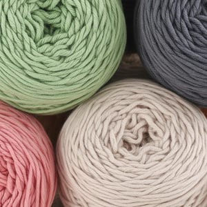 K&ouml;nnte beinhalten: Nahaufnahme von mehreren Wollkn&auml;ueln in verschiedenen Farben. Die Farben umfassen Hellgr&uuml;n, Grau, Rosa und Beige. Das Garn ist fest gewickelt, und die Textur des Garns ist sichtbar. Das Bild ist gut beleuchtet und die Farben sind lebendig. Das Garn ist wahrscheinlich f&uuml;r Strick- oder H&auml;kelprojekte.