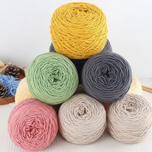 K&ouml;nnte beinhalten: Eine Sammlung bunter Wollkn&auml;uel in Gelb-, Gr&uuml;n-, Rosa-, Grau- und Beiget&ouml;nen. Das Garn ist ordentlich zu runden Kn&auml;ueln gewickelt, perfekt f&uuml;r Strick- oder H&auml;kelprojekte. Das Bild zeigt eine Vielzahl von Farben und Texturen.