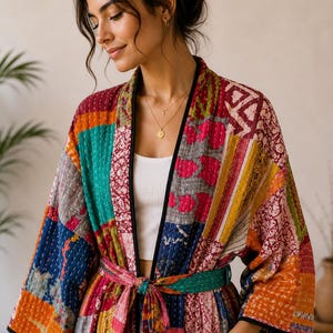 May include: A long-sleeved patchwork kimono robe featuring a vibrant mix of multicolored fabric panels with intricate stitching. The garment includes a matching tie belt at the waist, two front pockets, and black trim along the edges and collar.