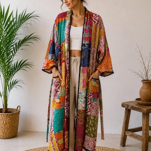 May include: A long, patchwork robe in a variety of colors, including orange, green, and pink. The robe has a black trim and pockets. The model is wearing the robe over a white top and beige pants. The robe is made of a soft, quilted material.