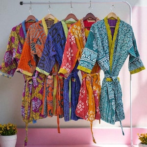 May include: Five colorful, patterned robes hang on a clothing rack. The robes feature various designs, including floral and geometric patterns, in shades of orange, blue, green, and purple. Each robe has a matching belt.