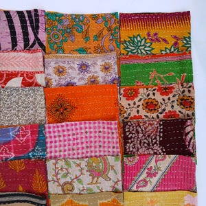 Könnte beinhalten: Ein Patchwork-Textil mit einer Vielzahl farbenfroher Stoffquadrate. Die Quadrate zeigen florale, geometrische und abstrakte Muster in Orange-, Rosa-, Lila- und Grüntönen. Die Teile sind mit weißem Faden zusammengenäht.