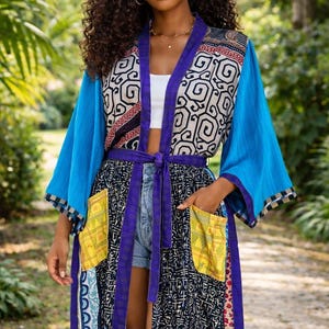 May include: A colourful, patterned kimono-style robe with blue sleeves and a geometric design on the upper section. The robe features a purple belt and pockets with yellow accents. The overall aesthetic is bohemian and vibrant.