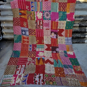 May include: A patchwork quilt with a vibrant mix of colors and patterns. The quilt features a variety of fabrics in shades of red, pink, green, and beige, arranged in a square pattern. The quilt is likely made of cotton and is suitable for a bed or sofa.