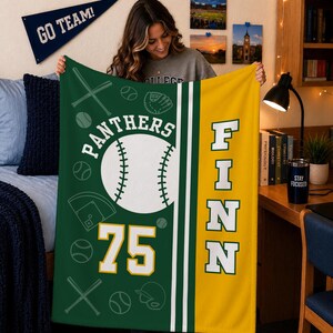 May include: A green and yellow fleece blanket featuring a large white baseball graphic, the text PANTHERS, the number 75, and the name FINN in bold white letters. The design includes scattered outlines of baseballs, bats, and a catcher's mitt.