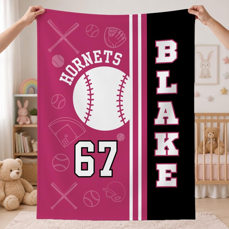 May include: A rectangular fleece blanket featuring a magenta left side with white baseball-themed graphics, including bats, balls, a glove, a helmet, and a home plate. The text reads HORNETS and 67. A black right side features the vertical text BLAKE.