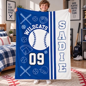 May include: A blue and white fleece blanket featuring a baseball theme with the text "WILDCATS", "SADIE", and the number "09". The design includes white line art of baseballs, bats, a glove, a helmet, and a diamond field on a blue background.