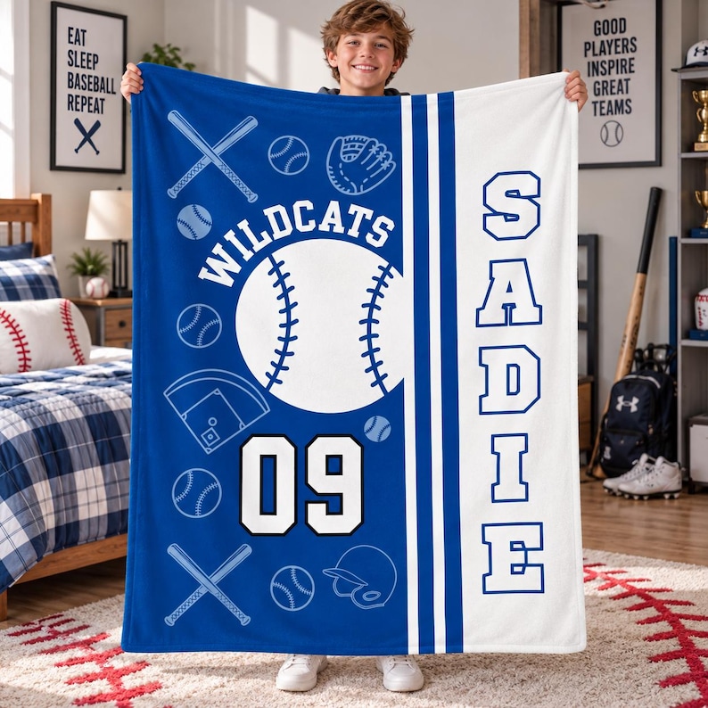May include: A blue and white fleece blanket featuring a baseball theme with the text "WILDCATS", "SADIE", and the number "09". The design includes white line art of baseballs, bats, a glove, a helmet, and a diamond field on a blue background.