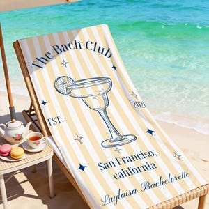 May include: Beach scene with a striped beach towel on a wicker lounge chair. The towel has a margarita glass graphic and text that reads "The Bach Club, San Francisco, California, Laylaisa Bachelorette."
