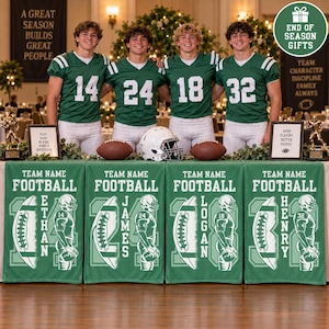 May include: Four football players in green jerseys with numbers 14, 24, 18, and 32 stand behind a table draped with four green banners. Each banner features a football graphic, a player silhouette, and the names Ethan, James, Logan, and Henry.
