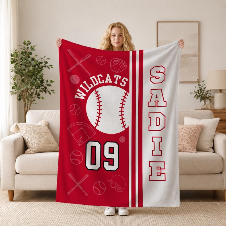 May include: A red and white fleece blanket featuring a baseball theme with the text WILDCATS and the number 09. The design includes baseballs, bats, a glove, and a field diagram. The name SADIE is printed vertically in large red block letters.