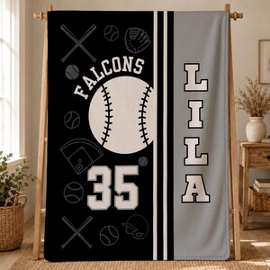 May include: A black and gray blanket featuring a large white baseball graphic, the text "FALCONS" arched above, the number "35" below, and the name "LILA" vertically in white block letters. The design includes baseball bats, balls, and gloves.
