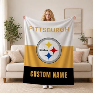 May include: A rectangular fleece blanket featuring a horizontal tri-color design of white, gold, and black. The top white section displays the text PITTSBURGH in gold. The center features the Steelers logo, and the bottom black section says CUSTOM NAME.