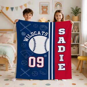 May include: A rectangular fleece blanket featuring a blue section with white baseball-themed graphics, the text "WILDCATS" and "09", and a red section with the name "SADIE" in large white block letters, separated by vertical white stripes.