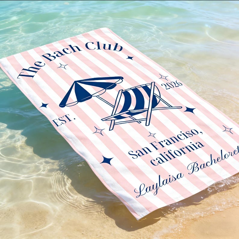 May include: Pink and white striped beach towel with navy blue illustrations of a beach umbrella and chair. The text "The Bach Club" and "San Francisco, California" are printed on the towel.