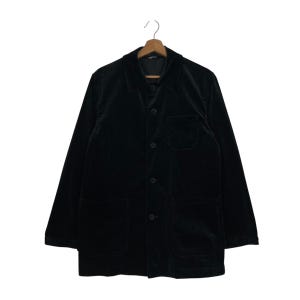 May include: A black corduroy jacket with a button-up front, a notched collar, and two large front pockets. The jacket is hanging on a wooden hanger against a white background. The jacket has long sleeves and a single chest pocket.