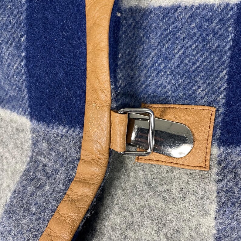 May include: Close-up of a blue, grey, and white plaid fabric with a tan leather strap and a silver metal buckle. The leather strap is stitched to the fabric. The buckle is rectangular.