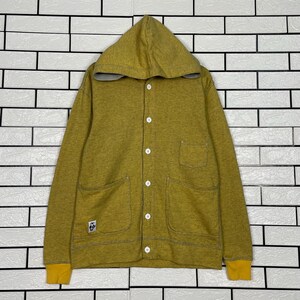 Peut inclure: Veste à capuche jaune moutarde avec boutons blancs, deux poches avant et poignets jaunes. La veste a une capuche doublée grise et un petit écusson logo sur le devant. Vêtement d'extérieur décontracté à boutons.