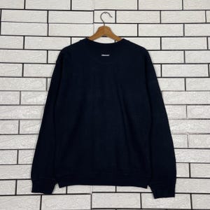 May include: A black long-sleeve sweatshirt with a small white logo near the neckline. The sweatshirt is hanging on a wooden hanger against a white brick wall. The logo appears to read "409-427".