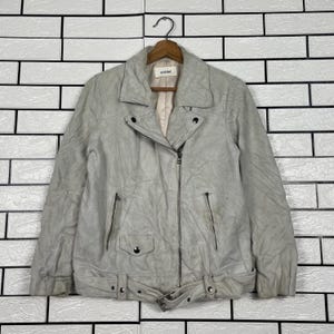 May include: A light gray, textured jacket with a notched collar, asymmetrical zipper closure, and a belted waist. The jacket features two zippered pockets and a small pocket with a button closure. The brand name "snidel" is visible on the label.