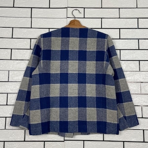 May include: A blue, grey, and brown plaid jacket hanging on a wooden hanger. The jacket features a classic plaid pattern in shades of blue and grey. The collar is brown. The jacket is displayed against a white brick wall.