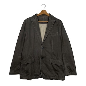 Peut inclure: Un blazer gris foncé avec deux poches avant et une fermeture à un seul bouton. La veste est suspendue à un cintre en bois. Le blazer a un revers cranté et une doublure de couleur claire.