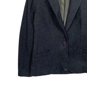 May include: A dark grey blazer with a single-button fastening and a notched lapel. The blazer features two front pockets and a subtle textured pattern. The interior lining is a muted green colour. The overall style is classic and tailored.
