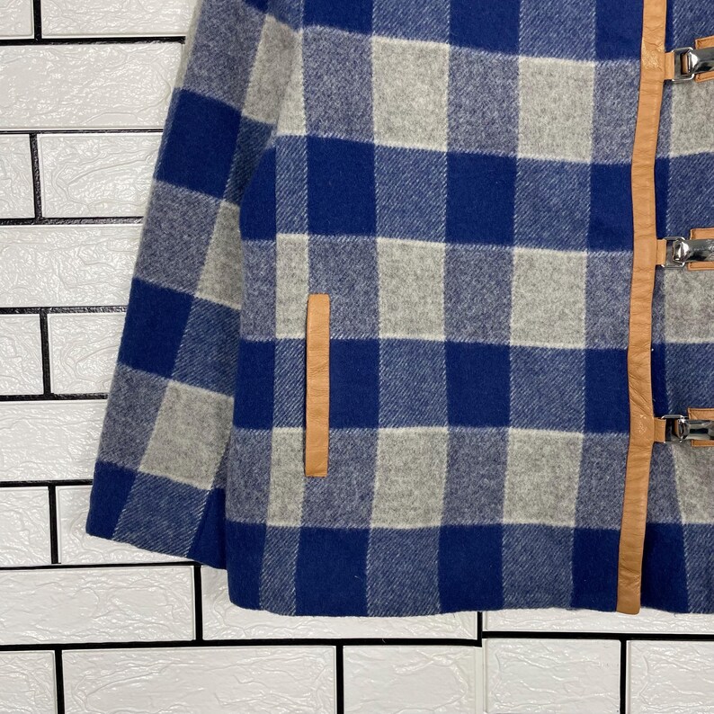 May include: A blue, grey, and white checked jacket with leather detailing and metal clasps. The jacket has a classic plaid pattern and a tailored fit. The leather accents add a touch of sophistication to the outerwear.
