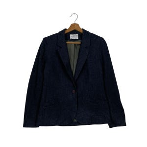 May include: A dark blue blazer with a single-button fastening, suspended from a wooden hanger. The blazer features a traditional notched lapel and a slightly textured finish. The interior lining is a muted green.