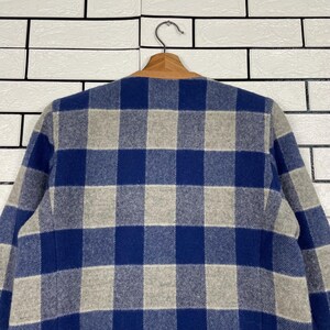 May include: A blue and grey checked jacket hanging on a wooden hanger. The jacket features a classic check pattern in shades of blue and grey. The collar is a light brown colour.