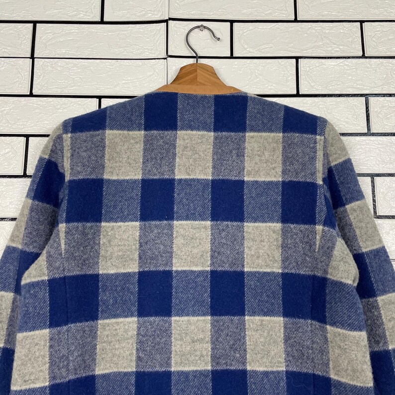 May include: A blue and grey checked jacket hanging on a wooden hanger. The jacket features a classic check pattern in shades of blue and grey. The collar is a light brown colour.