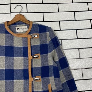 May include: A blue, grey, and white checked jacket with brown leather trim and silver clasps. The jacket is suspended on a wooden hanger. The brand name "Courr&egrave;ges" is visible on the label.