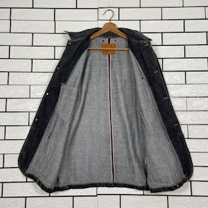 May include: A dark grey denim jacket hanging on a wooden hanger. The jacket is open, revealing a grey interior lining with a pink stripe down the centre. The jacket has two front pockets and button closures.