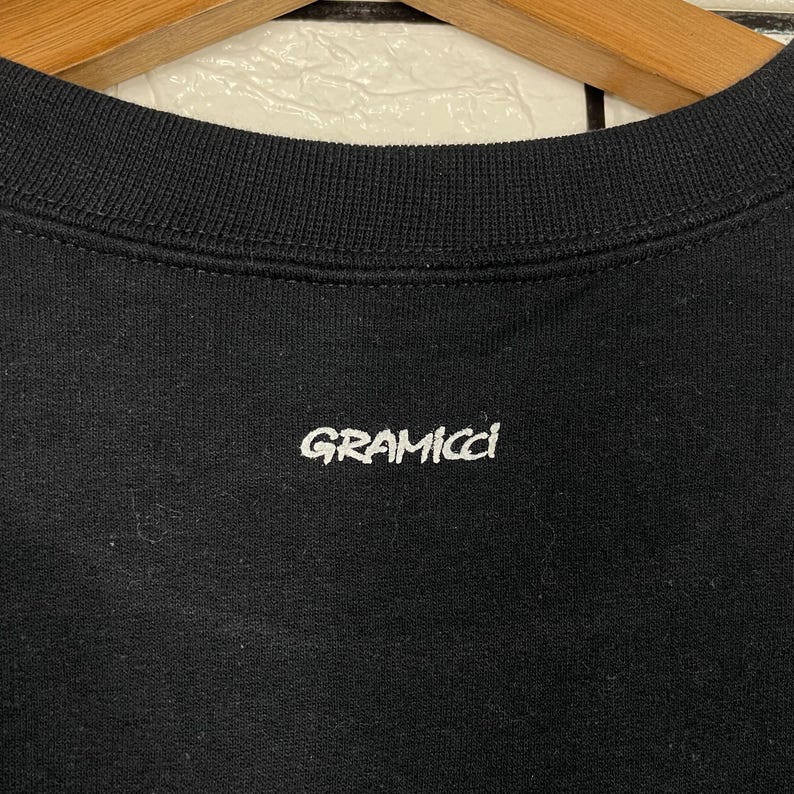 May include: Black crew neck sweatshirt with the white text "GRAMICCI" centered on the chest. The sweatshirt has a ribbed neckline. The fabric appears to be a soft, comfortable material.