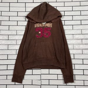 May include: Brown hooded sweatshirt with the text "Abercrombie 35" in a maroon color. The sweatshirt has a front pocket and a drawstring hood. The garment is made of a soft material.