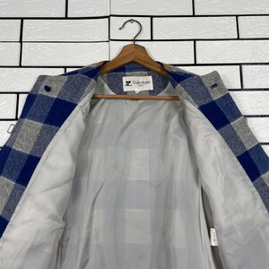 May include: A blue, grey, and white checked jacket with a light grey lining. The jacket is suspended on a wooden hanger. The brand name "Courr&egrave;ges" is visible on the label.