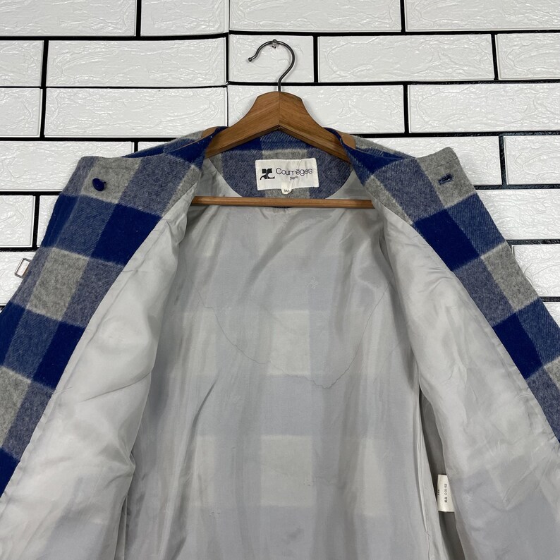 May include: A blue, grey, and white checked jacket with a light grey lining. The jacket is suspended on a wooden hanger. The brand name "Courr&egrave;ges" is visible on the label.