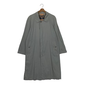 May include: A light gray trench coat with a classic design, featuring a collared neckline, button closure, and pockets. The coat is hanging on a wooden hanger. The interior lining has a plaid pattern.