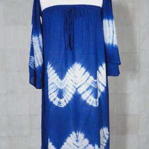 Puede incluir: Vestido azul teñido anudado con cuello cuadrado y mangas largas. El vestido presenta un patrón en zigzag blanco en la parte delantera y las mangas. El vestido se exhibe en un maniquí.