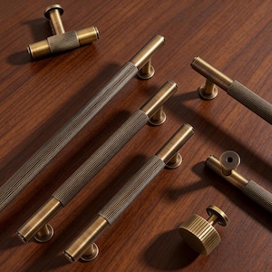 May include: A collection of antique brass cabinet pulls and knobs. The pulls have a ribbed center and are mounted on a wooden surface. The knobs and pulls are in various sizes and orientations, showcasing their design.