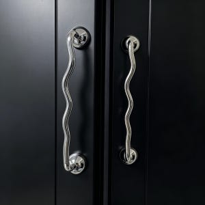 May include: Two wavy, polished chrome door handles are mounted on a black cabinet. The handles have a unique, organic shape, with a series of curves. The handles are attached to the cabinet with circular, chrome-finished mounts.