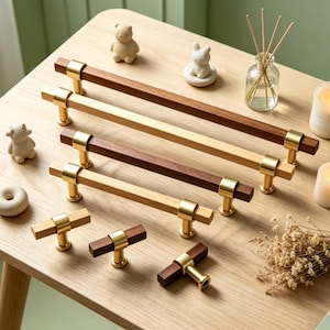 May include: A collection of wooden cabinet pulls and knobs in various sizes and finishes. The pulls feature a combination of light and dark wood with gold-toned metal accents. Decorative candles and small figurines are also present.