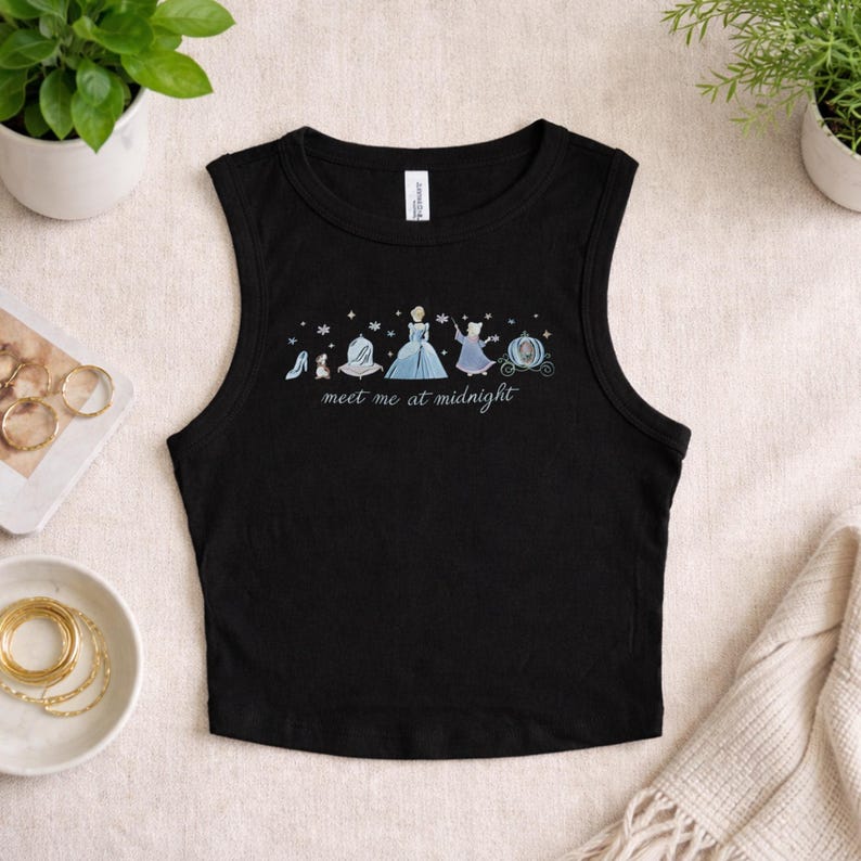 May include: Black sleeveless crop top with a whimsical illustration of Cinderella's iconic elements. The design includes a glass slipper, dress, and carriage, with the text "meet me at midnight".