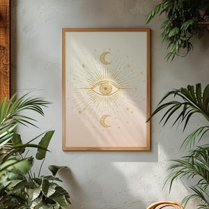 Pode incluir: Uma impressão de arte de parede retangular numa moldura de madeira clara com um símbolo de olho dourado central rodeado por linhas radiantes, com uma lua crescente posicionada acima e abaixo do olho, num fundo de gradiente suave.