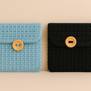 May include: Two handmade crochet pouches. One is light blue, the other is black. Each has a flap secured with a round, light-coloured wooden button. The pouches are made with a thick, textured yarn, suggesting a sturdy construction.