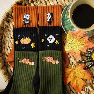 May include: Halloween-themed socks with embroidered pumpkins, stars, and cartoon characters. The socks are black, orange, and green, displayed on a woven tray with a coffee cup, autumn leaves, and a candle. The tray is 30 cm in diameter.