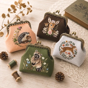May include: Four coin purses with antique brass kiss-lock frames. One peach purse features a hedgehog, a brown purse shows a deer with flowers, a green purse displays a raccoon, and a light grey purse depicts a rabbit surrounded by a floral wreath.