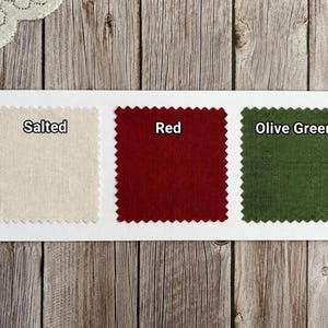 May include: Three square fabric swatches with pinked edges arranged horizontally on a white rectangular card. The swatches are labeled Salted, which is a light beige, Red, and Olive Green. Each swatch displays a distinct solid color.